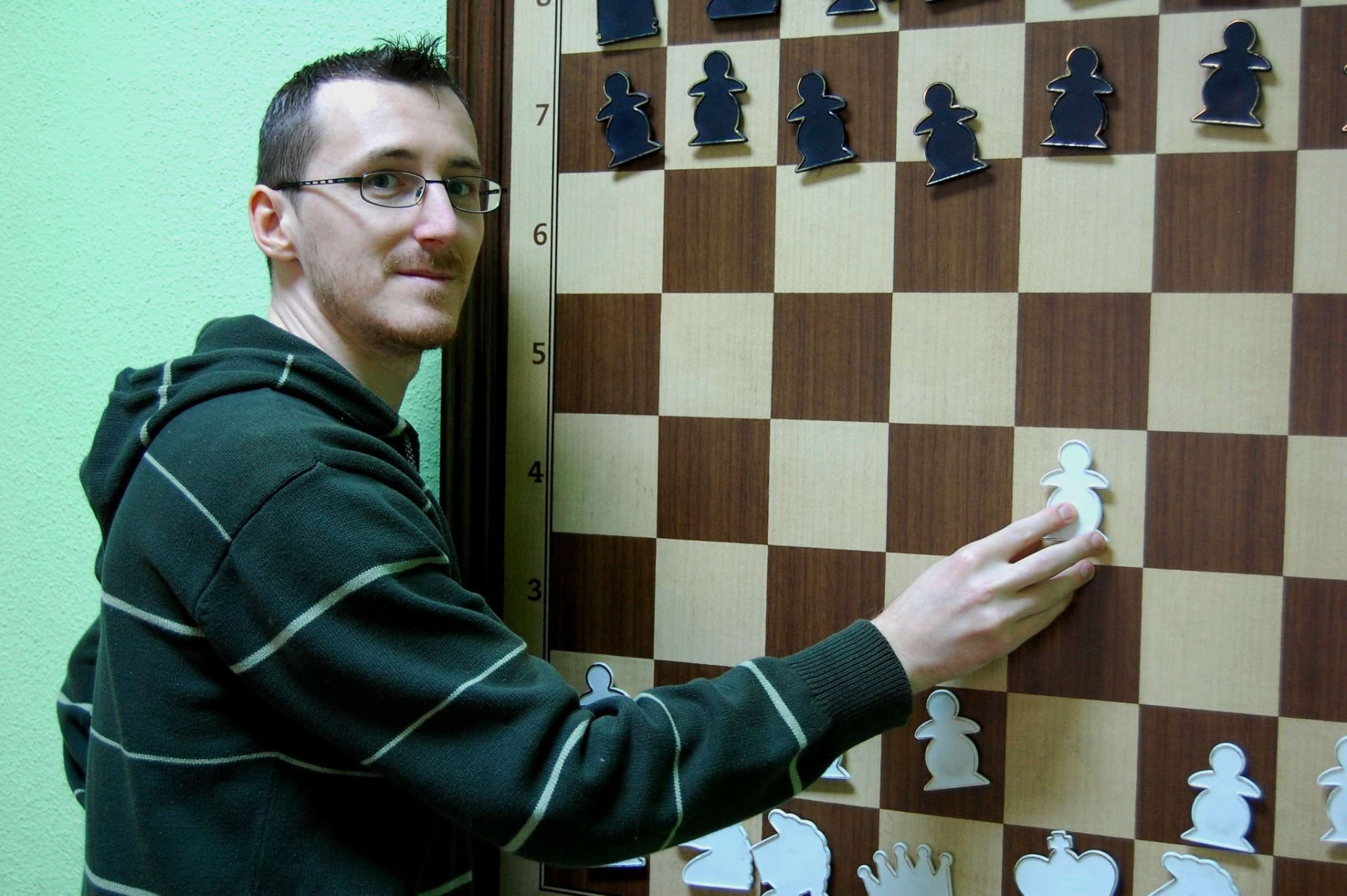 Chess player demonstrating a move on a large wall-mounted chessboard
