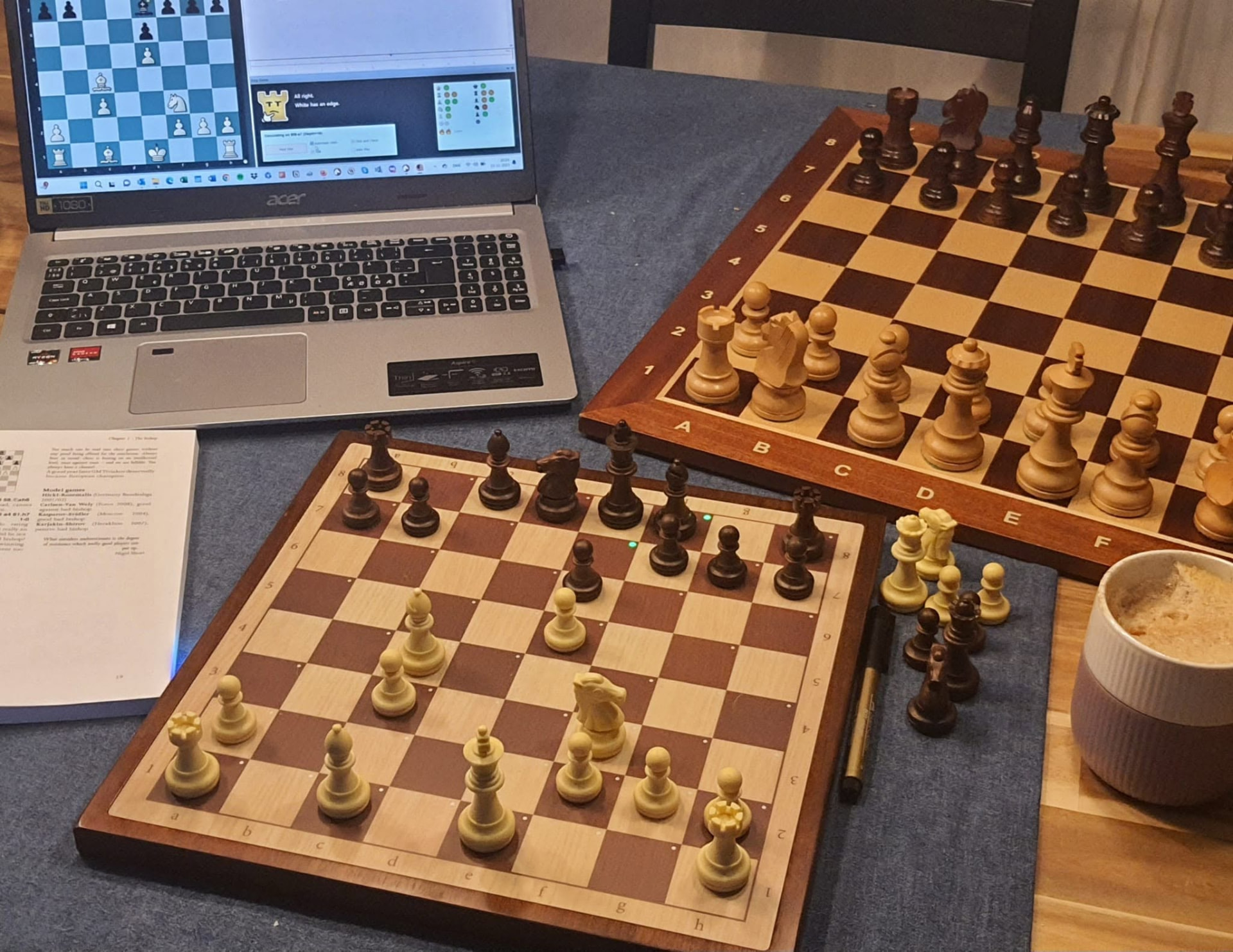 Chess study setup with physical boards, a laptop and a book