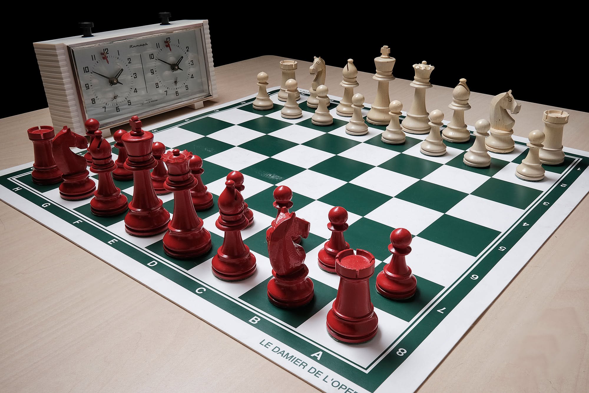 Classic red and white chess pieces set beside a tournament clock